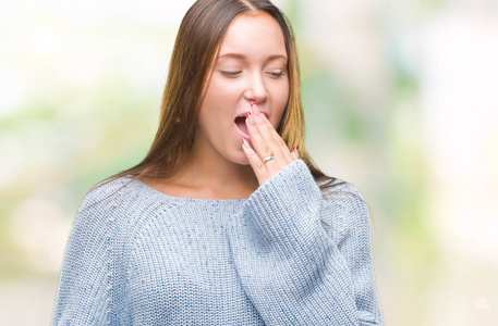 年轻漂亮的白种人女人穿着冬天的毛衣，在孤立的背景下，无聊地打哈欠，累得用手捂住嘴。 不安和困倦。