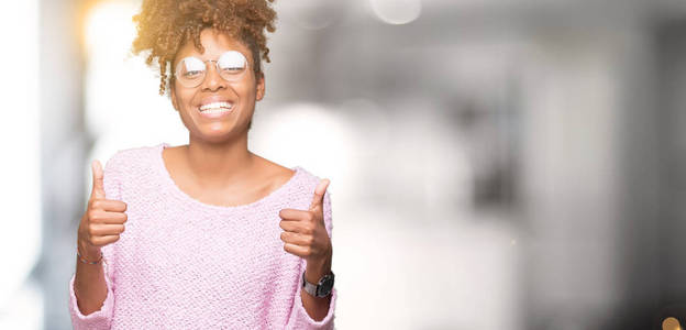 美丽的年轻非洲裔美国妇女戴着眼镜，在孤立的背景上，成功标志，用手竖起大拇指，微笑和快乐地做积极的手势。 用欢快的表情看着相机，胜