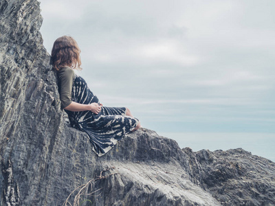 一个年轻女子坐在海边的岩石上