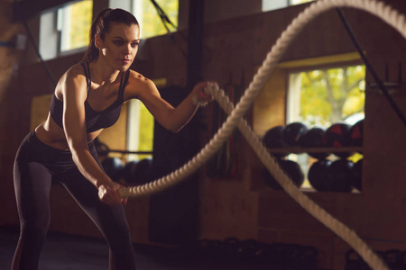 适合运动和运动的女运动员在健身房工作。 使用战斗绳训练妇女。 体育竞技生活方式和健身理念。