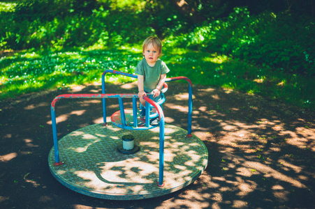 一个可爱的小男孩坐在公园里的旋转木马上