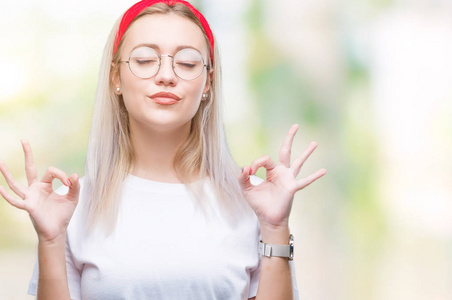 年轻的金发女人戴着眼镜在孤立的背景上放松和微笑，闭着眼睛做冥想手势用手指。 瑜伽概念。