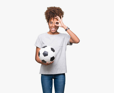 年轻的非洲裔美国妇女拿着足球球在孤立的背景上，快乐的脸，微笑着，做着好的标志，用手盯着手指看