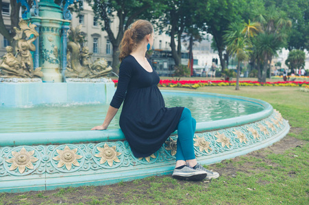 一位年轻女子坐在公园的喷泉旁