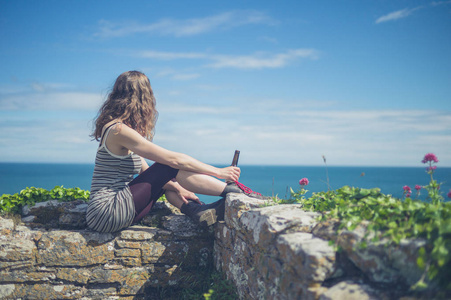 夏天，一个年轻的女人拿着一瓶啤酒坐在海边的墙上