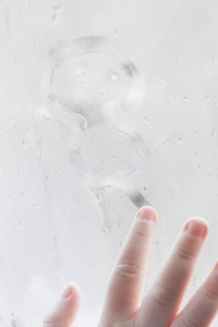 s hand draws a man on a frozen misted window in winter