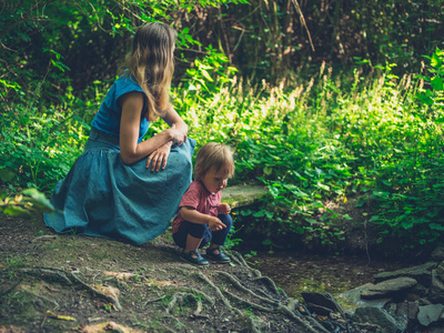 一位年轻的母亲和她蹒跚学步的孩子正在树林里的小溪旁放松