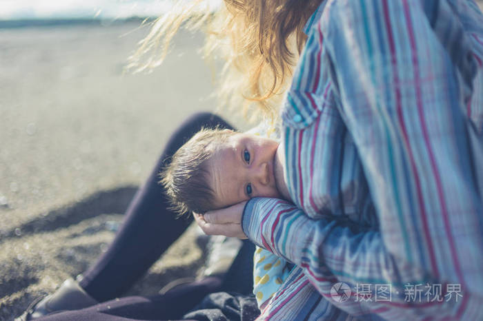 一位年轻的母亲正在海滩上给婴儿喂奶