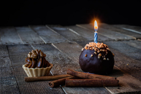 在木制厨房桌子上用蜡烛品尝纸杯蛋糕。 黑暗的背景。