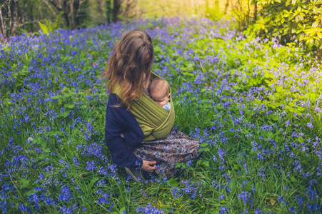 一位年轻的母亲带着一个熟睡的婴儿坐在蓝铃草甸里