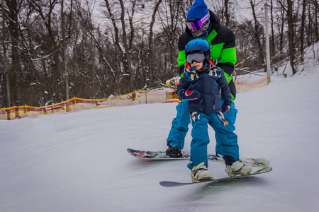 父亲滑雪板教儿子骑在木板上。