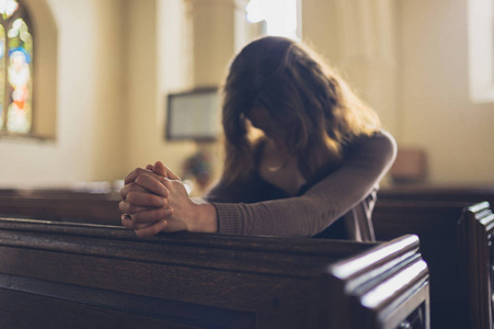 一位年轻女子双手交叉坐在教堂里祈祷