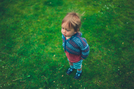 一个蹒跚学步的小男孩站在绿色的草坪上