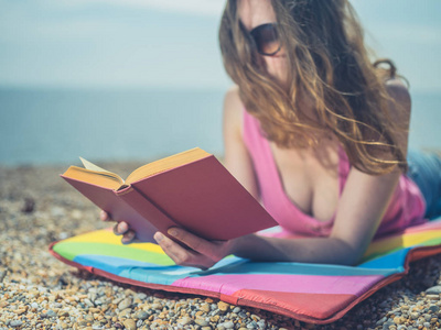 一位年轻女子躺在沙滩上，正在夏天阳光明媚的日子里看书