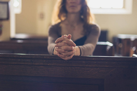 一位年轻女子双手交叉坐在教堂里祈祷