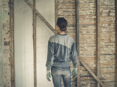 一个年轻的女人站在阁楼的房间里，正在看她把墙上的绝缘材料