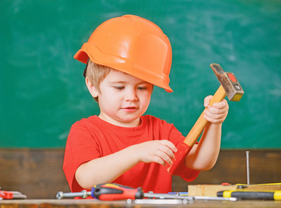 玩工具的孩子。在维修车间里, 身穿橙色头盔和红色 t恤的男孩坐在桌子后面