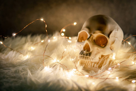 人类头骨在白色的弗卢尔地毯上装饰着圣诞灯。 万圣节节日概念摄影棚拍摄