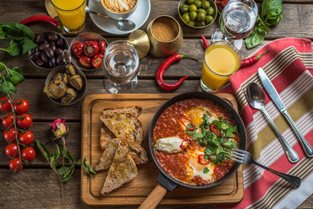 早餐与沙克舒卡橄榄，辣椒，西红柿，面包，果汁和咖啡在乡村木制桌子上。