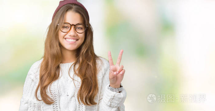 年轻漂亮的深色头发的女人戴着眼镜和冬天的帽子，戴着孤立的背景，用手指举着第二个手指，微笑着自信和快乐。