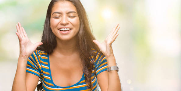 年轻美丽的阿拉伯女人在孤立的背景上庆祝疯狂和疯狂的成功，举起手臂和闭上眼睛尖叫兴奋。 赢家概念