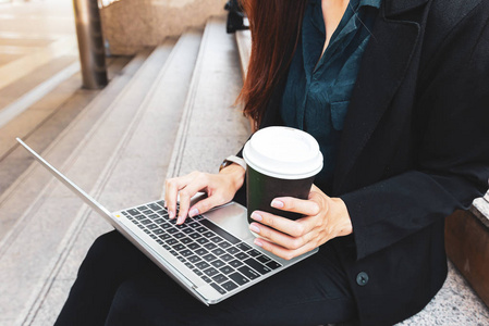 快乐的商务女性工作与笔记本电脑和持有咖啡杯在户外。 业务概念