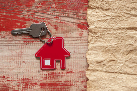在木制背景上关闭房子形状的钥匙链上的房子钥匙。 房地产概念搬迁住宅或租用红木物业