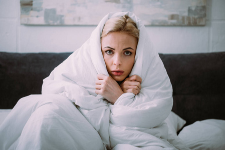 被吓得浑身裹着毯子的女人在床上看着摄像机照片