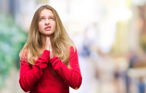 年轻漂亮的金发女人穿着红色毛衣，在孤立的背景下乞讨和祈祷，双手一起祈祷，脸上充满希望的表情，非常情绪化和担忧。 请求原谅。 宗教