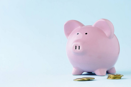 粉红色的小猪脸在蓝色的背景上，有复制空间，在金融投资和储蓄的概念中，前景是分散的硬币。