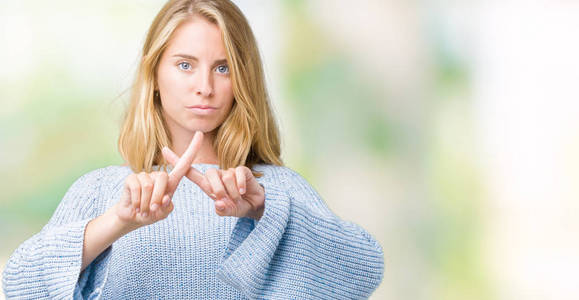 穿蓝色毛衣的漂亮年轻女子被孤立的背景排斥表情交叉手指做负号