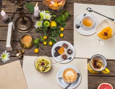 在木桌上放一杯卡布奇诺茶和甜点，上面有柑橘类水果和树叶
