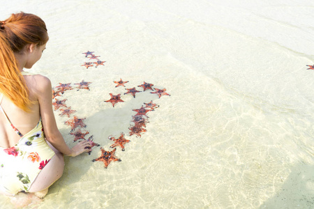 旅游女孩与海星一起为情人节做一颗心，蜜月在普吉岛，清澈的水和白沙滩