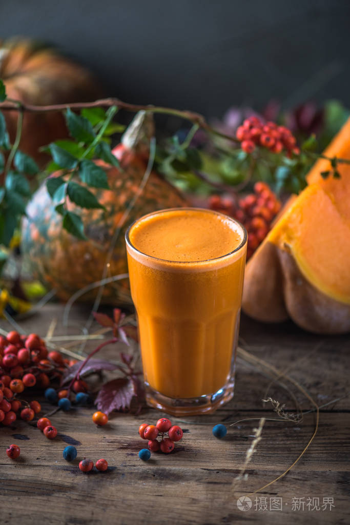 新鲜南瓜冰沙放在木桌上,上面有秋叶和浆果