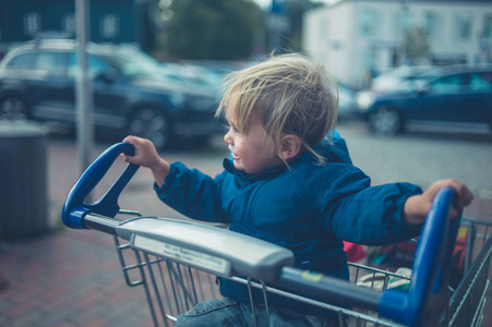 一个小蹒跚学步的孩子骑在购物车里玩得很开心