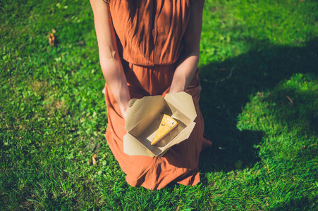 一个年轻的女人坐在草地上，盒子里放着一块蛋糕