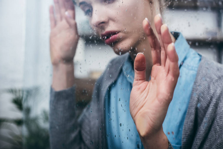 家中悲伤的成年女人用雨滴触摸窗户的画面