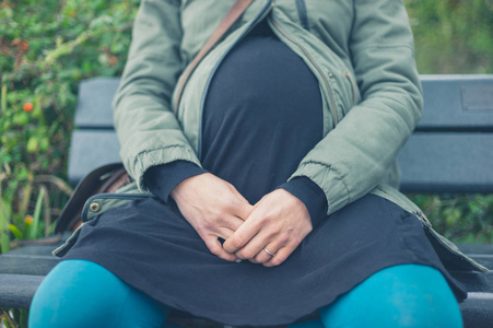 一位年轻的孕妇坐在外面的长凳上