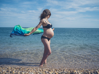 一位年轻的孕妇站在海滩上，一条沙龙在风中飘扬