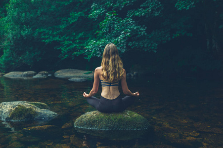 一位年轻女子正在河中的一块岩石上冥想