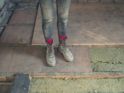 一个工人的脚和腿站在一个新的地下，在一个阁楼，正在绝缘羊毛类型的绝缘。