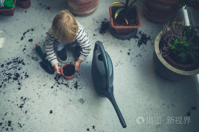 一个小蹒跚学步的孩子正在玩土和浇水罐