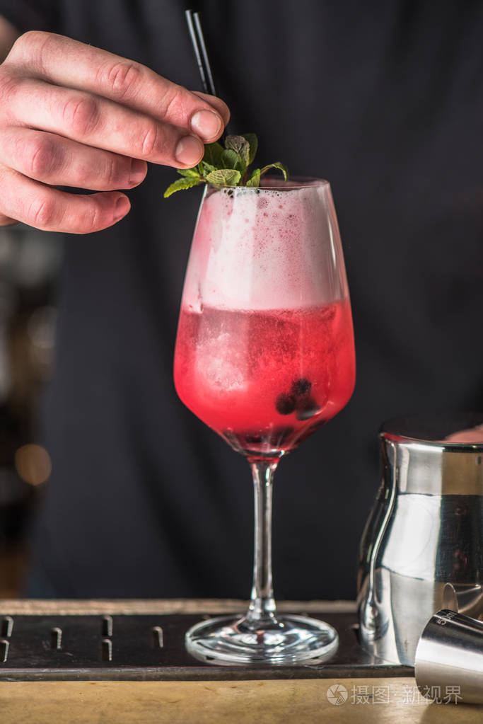 酒保用玻璃装饰粉红色鸡尾酒的手