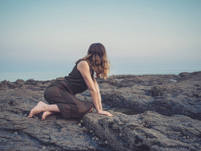 日落时分，一位年轻女子正坐在海岸上的一个岩石池旁