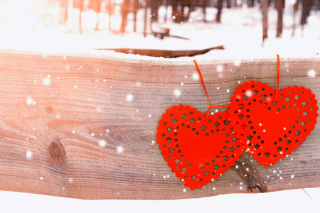 两个红色的心在一个老式的木板上, 在阳光和雪的冬天森林。情人节贺卡