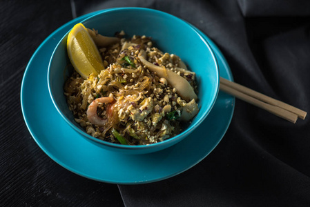 一碗亚洲海鲜面条，放在盘子里，柠檬和筷子放在黑色织物上