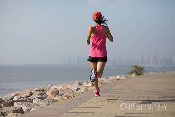 健身女运动员在阳光明媚的海岸跑步