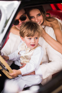 这对幸福微笑的新婚夫妇和一个小男孩坐在车里拥抱着
