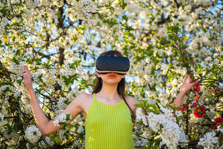 最好的虚拟现实。可爱的女孩在春天的花园玩。年轻的女士戴春天的大自然。漂亮的女孩在虚拟现实耳机。创新的 vr 技术。虚拟技术仿真