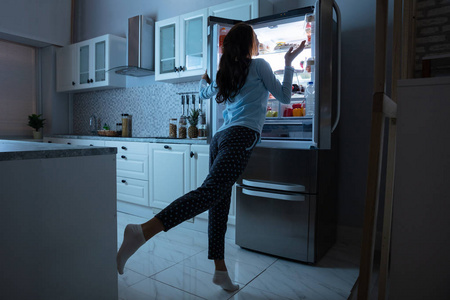 女人打开冰箱门，厨房里有各种食物